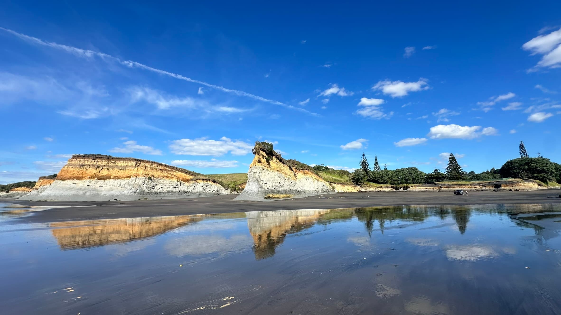 Coastal cliffs reflected on wet sand at Onaero Beach, Taranaki, New Zealand